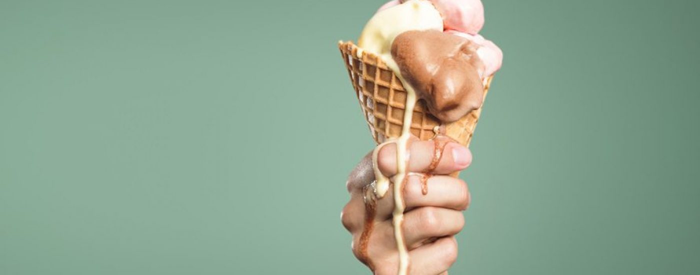 Ice cream in a cone held by a hand is dripping as it melts away.  Panoramic version with a lot of copy space.