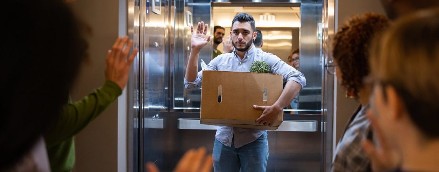 Man being fired at his job and looking sad leaving the office saying goodbye to his colleagues